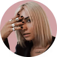 Blonde woman with straight hair covering one eye with fingers adorned in silver rings.