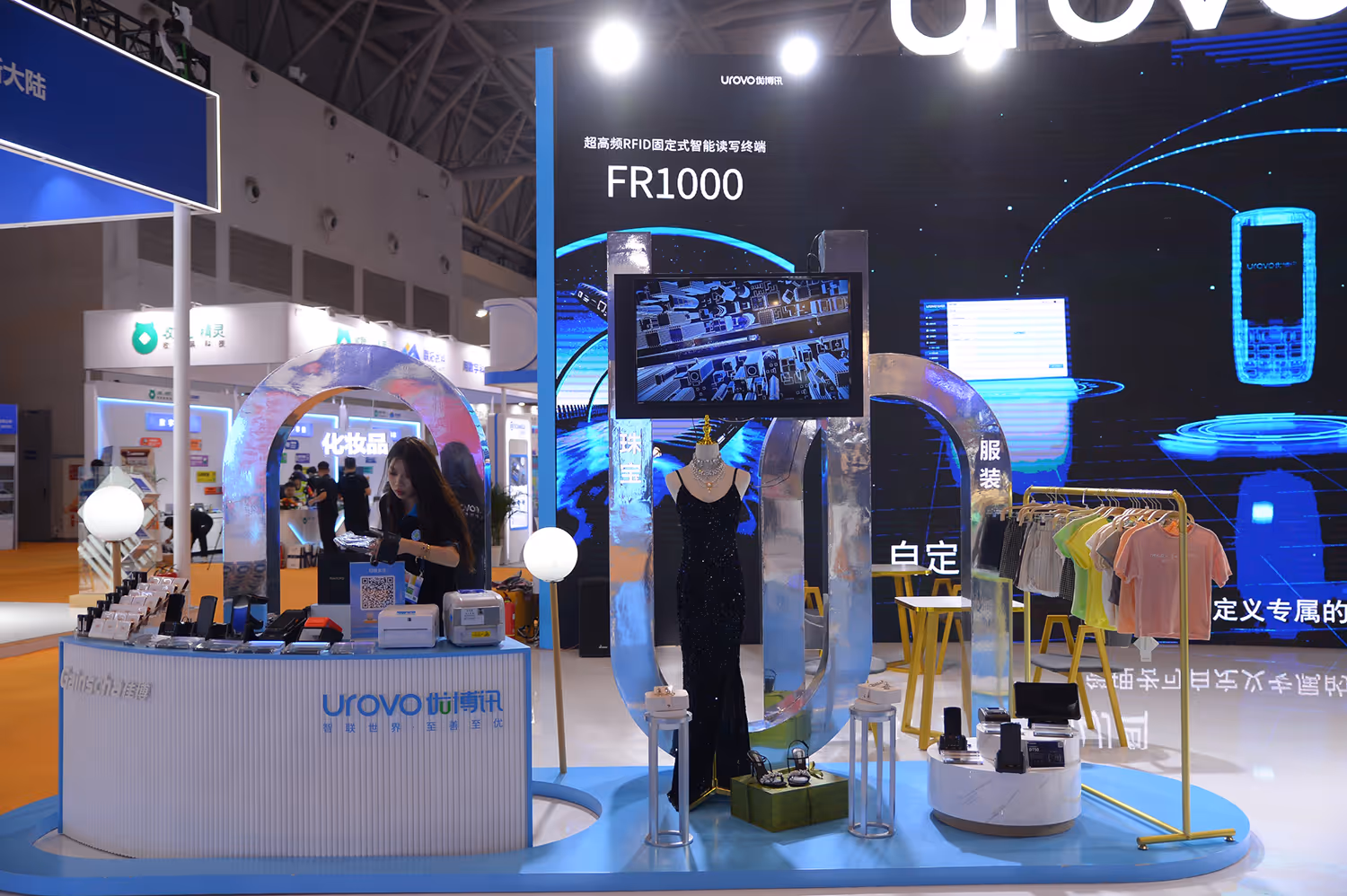 Display of various bottled drinks and packaged products on a white counter at a trade show or store.