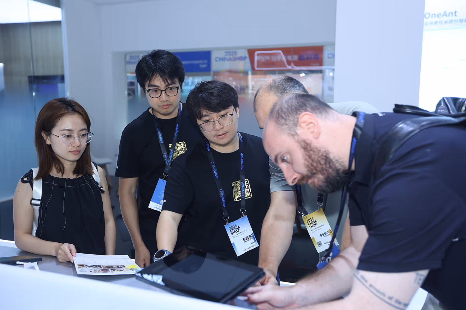 Group of five people at a trade show booth looking at a tablet, with some wearing 2025 China Shop badges.