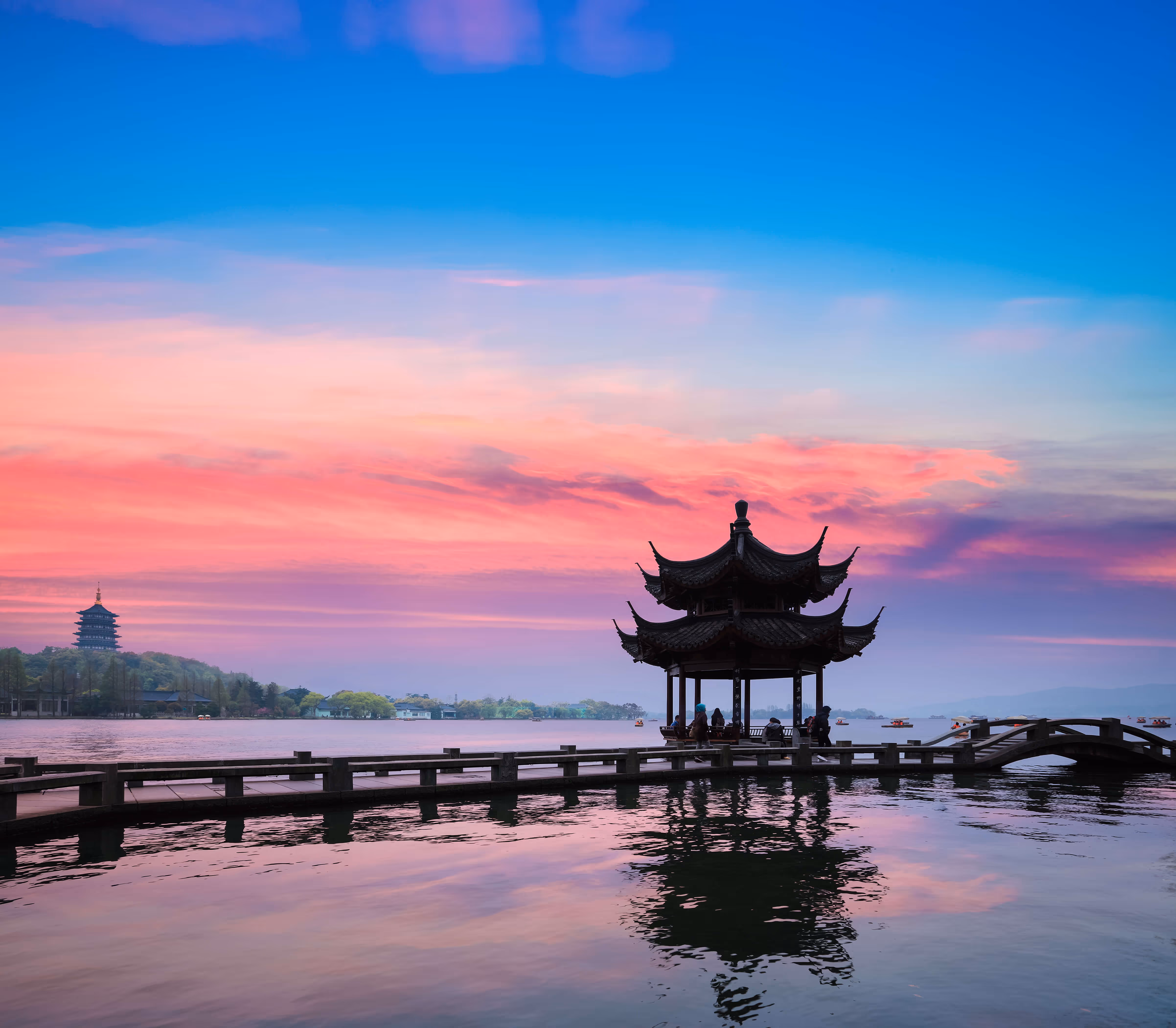 Traditional Chinese pavilion on a pier over calm lake water during a vibrant pink and blue sunset.