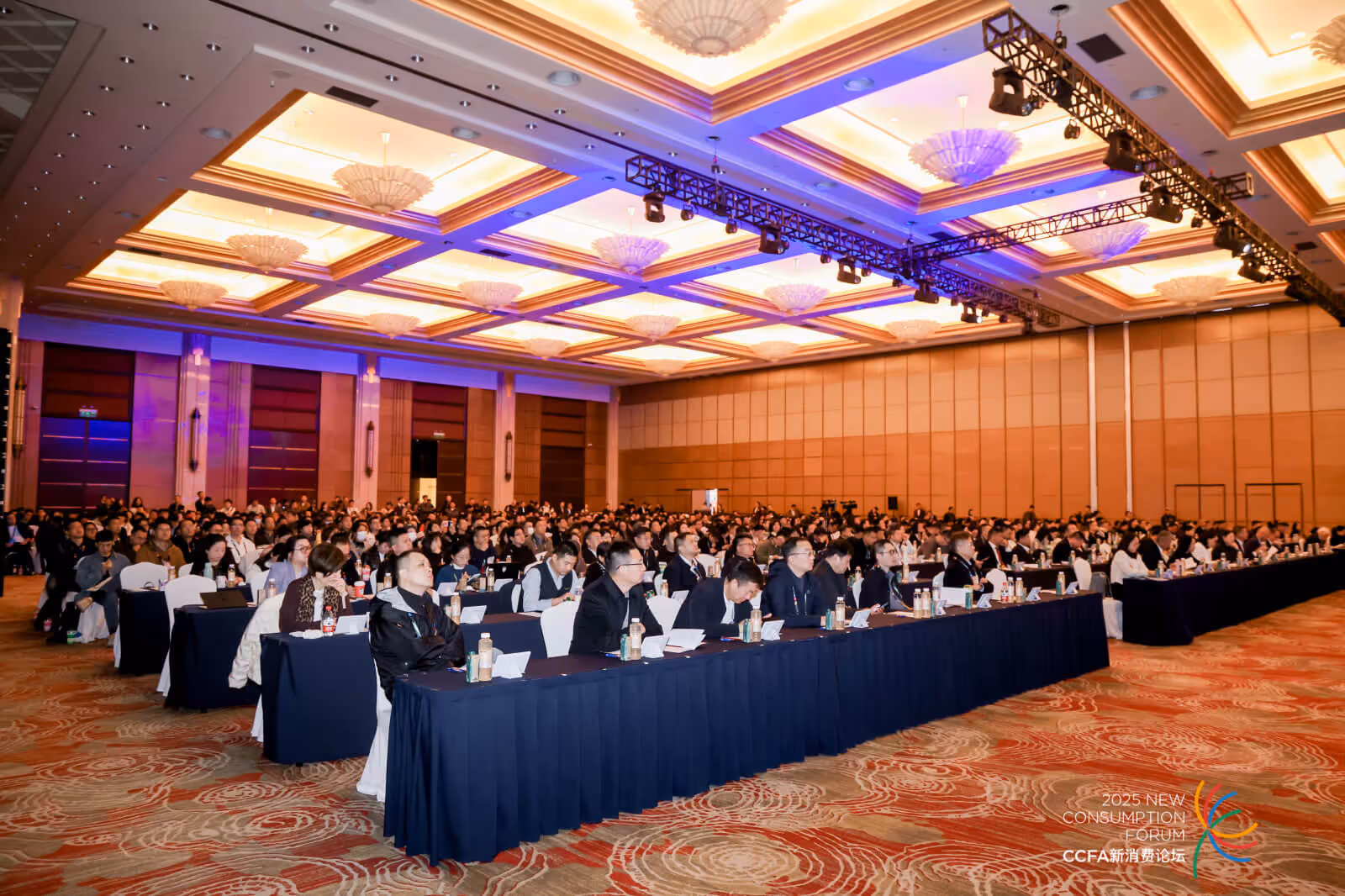 Large audience seated at long tables in a brightly lit conference hall during the 2025 New Consumption Forum.