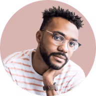 Portrait of a thoughtful man with glasses and a beard, resting his chin on his hand against a pink background.