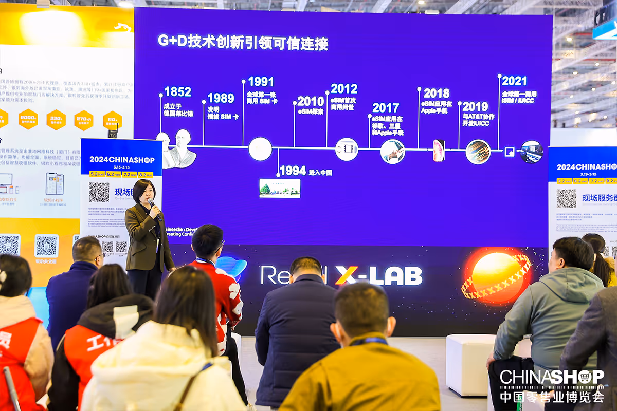 Speaker presenting in front of an audience with a large timeline display about G+D technology innovation at a conference.
