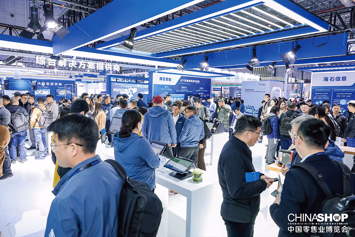 Crowded exhibition hall with people engaging around tech displays at ChinaShop retail industry expo.