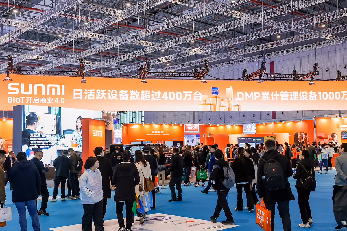Crowded tech exhibition hall with people walking around and an orange Sunmi booth displaying digital and software solutions.