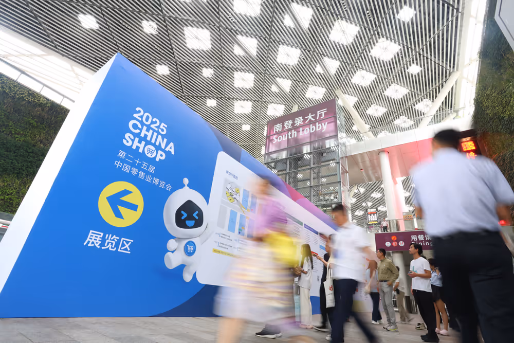Indoor scene at the South Lobby showing a large blue sign for the 2025 China Shop exhibition with people walking by in motion blur.