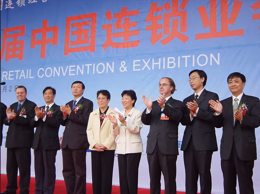 A group of eight formally dressed individuals standing in a row on a red carpet in front of a blue backdrop with large red and white text reading 'Retail Convention & Exhibition' and Chinese characters.